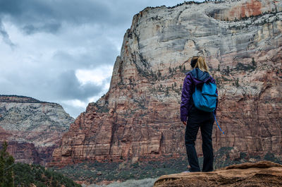 Rear view of hiker standing on rock against mountain during weather