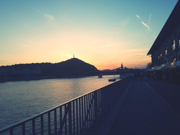 Bridge over river by buildings against sky during sunset