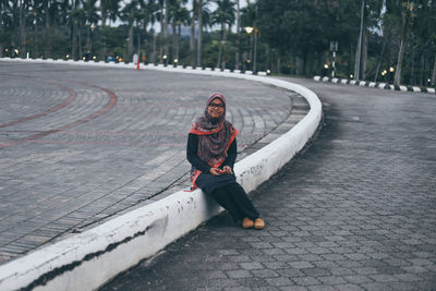Portrait of smiling young woman sitting on dividing line at street