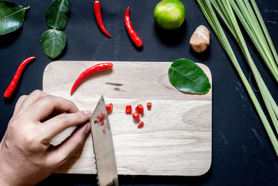 High angle view of hand holding red chili peppers on cutting board