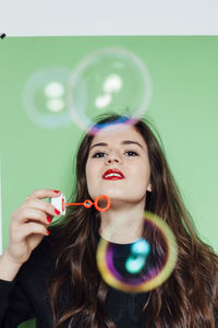 Portrait of young woman blowing bubbles against green background