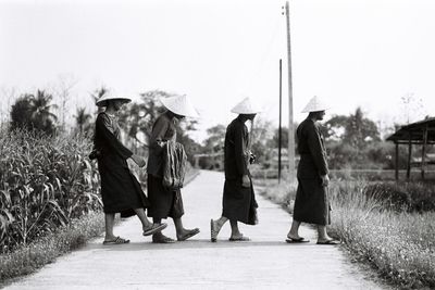 Side view of men wearing asian style conical hats while walking on road against clear sky