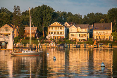 Sailboats in lake against houses and trees in city