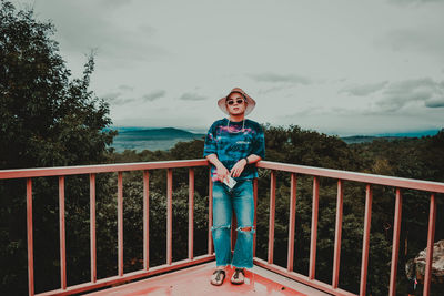 Portrait of boy standing on railing against sky