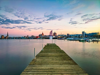 Pier on river against sky during sunset