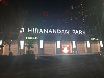 Information sign on illuminated road by buildings at night