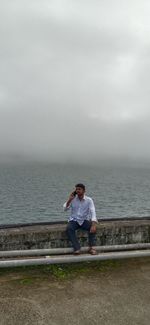 Man sitting on sea shore against sky