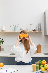 An attractive girl smiles and closes her eyes with orange halves in the kitchen. the concept of diet