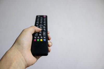 Cropped hand of person holding remote control against wall at home