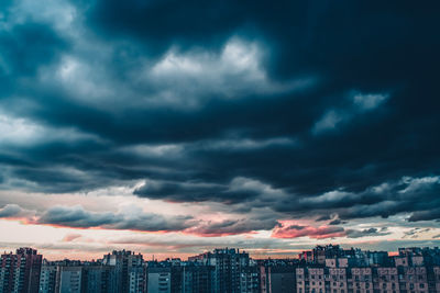 Cityscape against cloudy sky in city at sunset