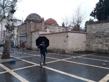 Full length of man standing by building against sky during rainy season