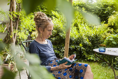 Senior woman with dreadlocks sitting in the garden looking at personal organizer