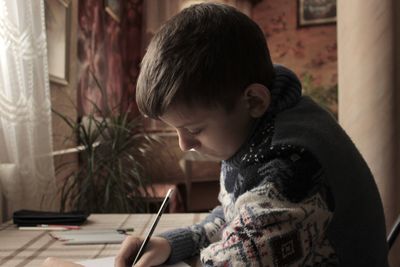 A boy in a christmas sweater sits at the table and draws and writes