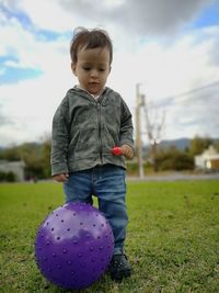 Low angle view of cute baby boy with ball standing on grassy field