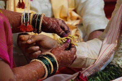 Cropped hands of bride tying thread on bridegroom during wedding ceremony