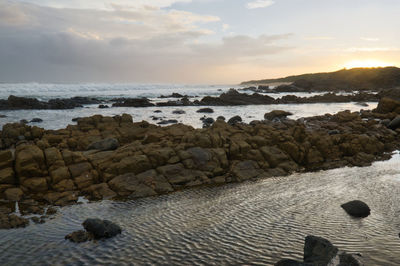 Rocks on beach against sky during sunset