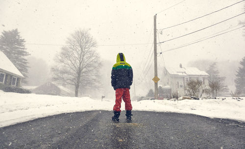 Rear view of boy standing on road by snow covered land during winter