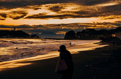 Woman standing on beach against sky during sunset