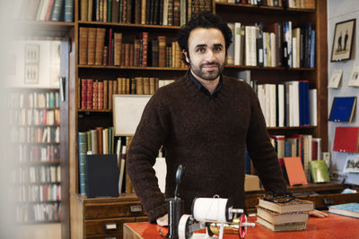 Portrait of smiling librarian standing against bookshelves
