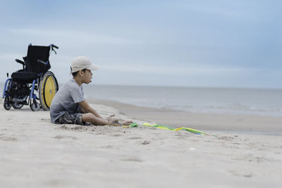 Man sitting on shore at beach against sky