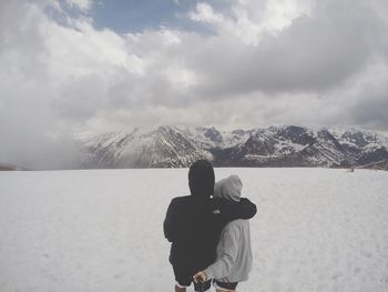 Rear view of couple photographing on snow covered field by mountains against cloudy sky