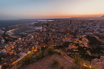 Aerial view of cityscape by sea against sky at sunset