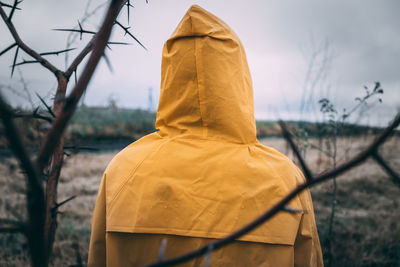 Back of man yellow cloak cloudy rainy weather branches tree with thorns. trouble expectation concept