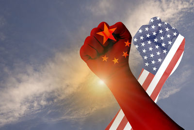 Low angle view of hand holding flag against sky