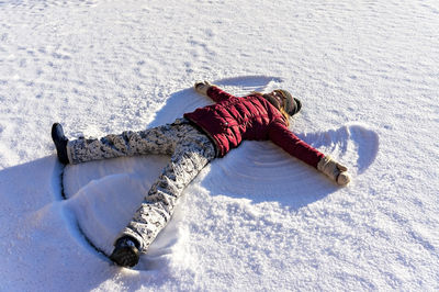 Young woman lying in the snow and making a snow angel. winter walks and fun, holidays