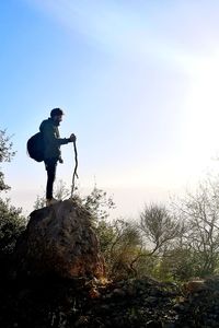 Side view of man standing on rock against sky