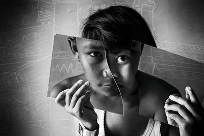 Portrait of girl holding broken glass in front of face with reflection of boy at classroom