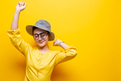 Woman wearing novelty glasses and hat against yellow background