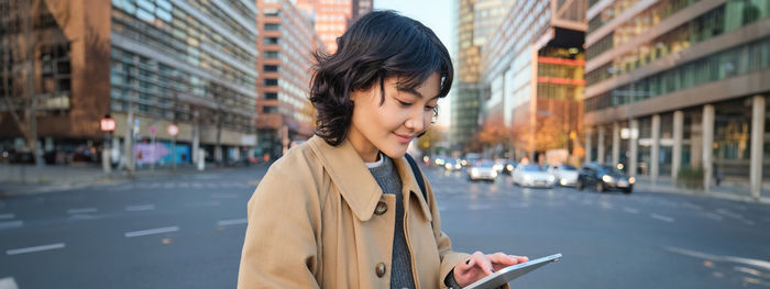 Young woman using mobile phone while standing in city