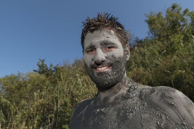 Portrait of man with mud on body against blue sky