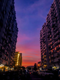 Illuminated city street and buildings against sky at sunset