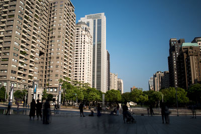 People on street amidst buildings in city against clear sky