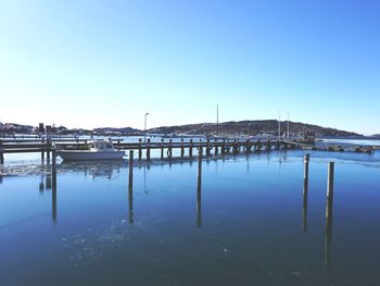 Reflection of boat and wooden post in sea against blue sky