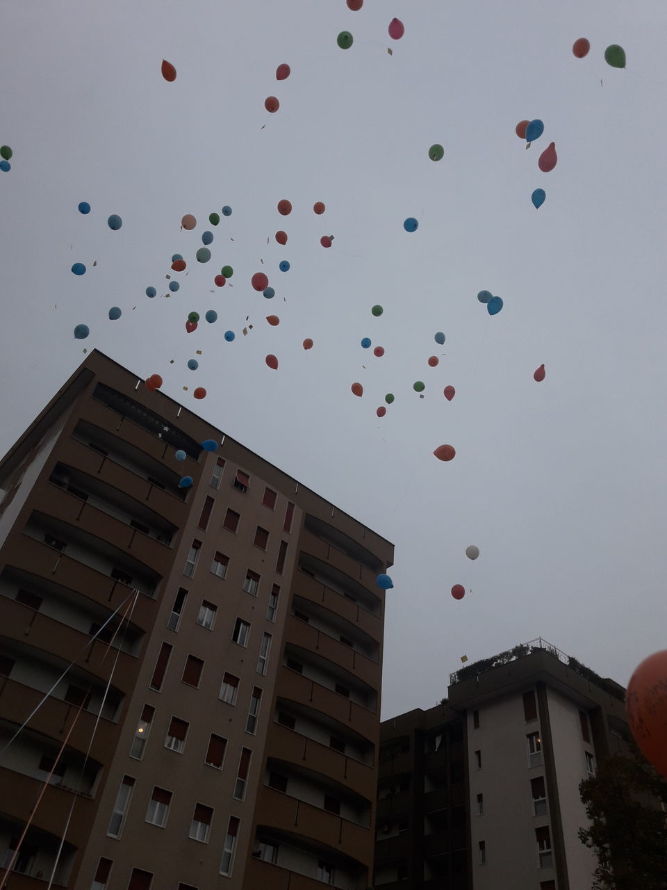 LOW ANGLE VIEW OF BALLOONS FLYING OVER BUILDINGS AGAINST SKY