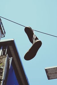 Low angle view of shoes hanging against clear blue sky