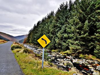 Road sign by trees against sky