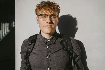 Portrait of blond male student wearing eyeglasses holding book against gray wall