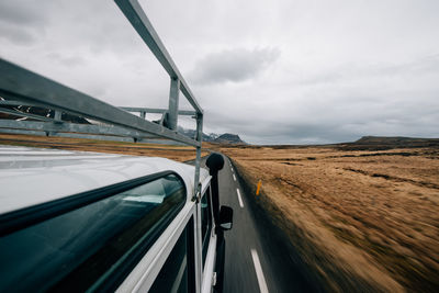 Car moving on road against cloudy sky