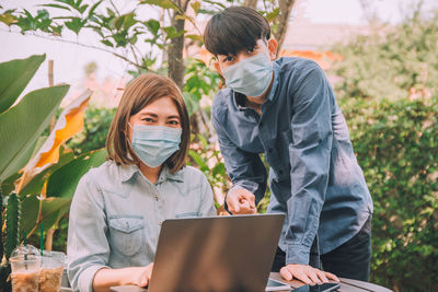 Portrait of business people wearing mask using looking at laptop outdoors