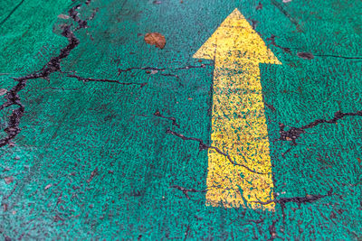 High angle view of yellow arrow symbol on turquoise footpath