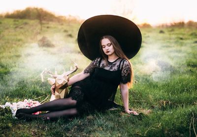 Young woman sitting on field against sky