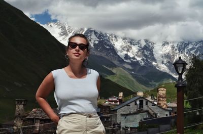 Young woman wearing sunglasses standing on mountain against sky