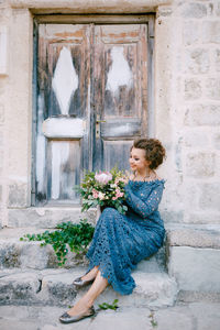 Full length of bride holding flower bouquet sitting by door