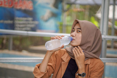 Asian muslim woman wearing a beautiful hijab is drinking bottled water in the park