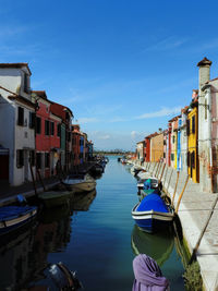 Boats moored in canal amidst buildings against sky