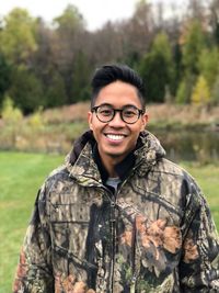 Portrait of smiling young man standing against trees in forest